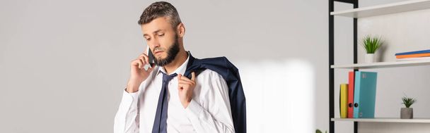 Biznesmen trzyma kurtkę podczas rozmowy na smartfonie w biurze, baner  - Zdjęcie, obraz