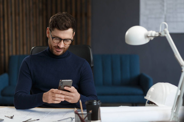 Young man using smartphone and smiling. Happy businessman using mobile phone apps, texting message, browsing internet, looking at smartphone. Concept of young people working with mobile devices - Foto, Bild