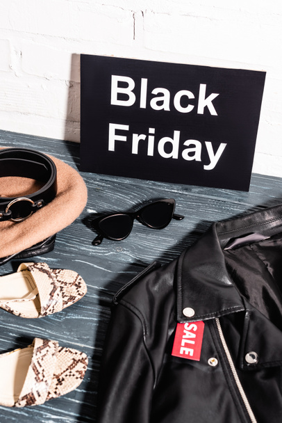 schoenen, zonnebril, baret en riem nabij boord met zwarte vrijdag en tag met uitverkoop belettering op leren jas  - Foto, afbeelding