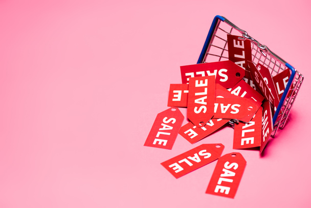 sale tags near shopping basket on pink, black friday concept  - Photo, Image