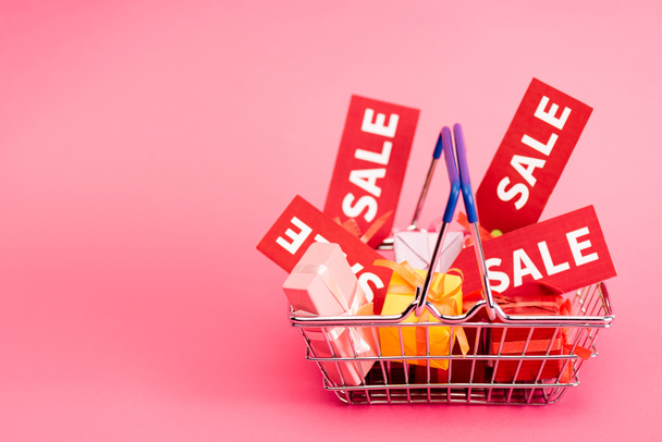 shopping basket with presents and red sale tags on pink  - Photo, Image