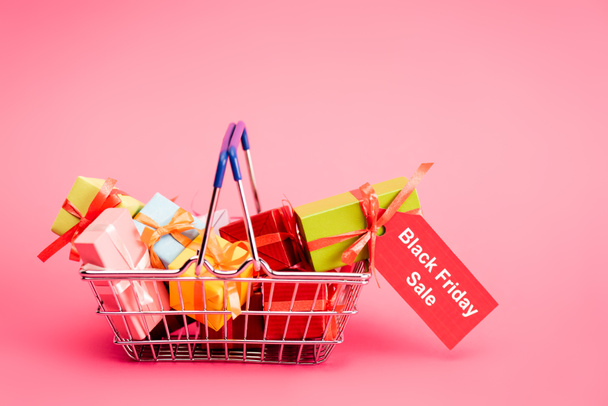shopping basket with presents and red tag with lettering on pink, black friday concept  - Photo, Image