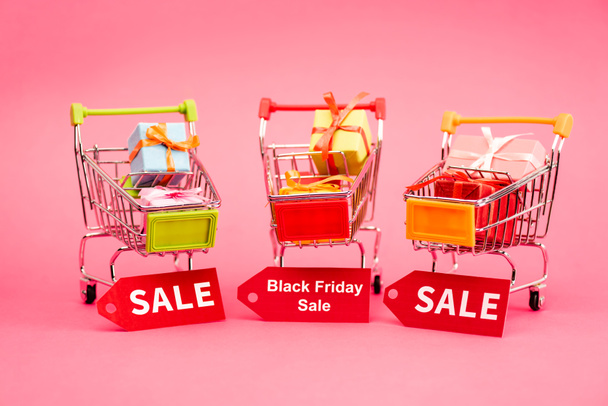 cadeaux colorés dans les chariots avec des étiquettes de vente sur rose, concept vendredi noir  - Photo, image