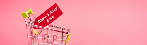 horizontal concept of red tag with black friday sale lettering in shopping cart isolated on pink  - Photo, Image