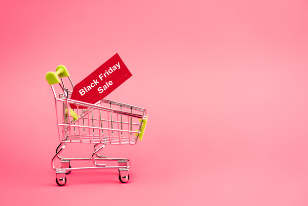 red tag with black friday sale lettering in shopping cart on pink  - Фото, изображение