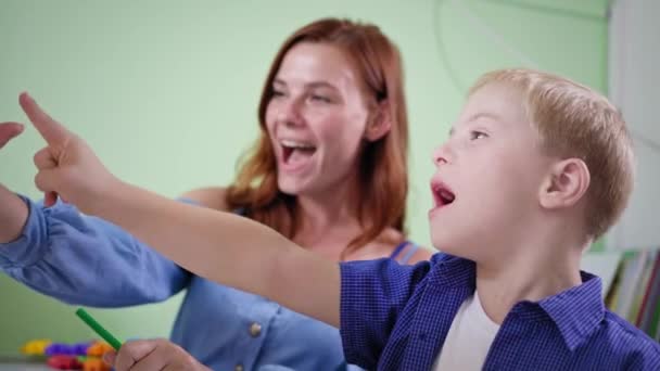 емоційний хлопчик з синдромом Даунса, дитина радіє успіху дає п'ять мамі і оплесках під час виконання домашнього завдання в кімнаті
 - Кадри, відео