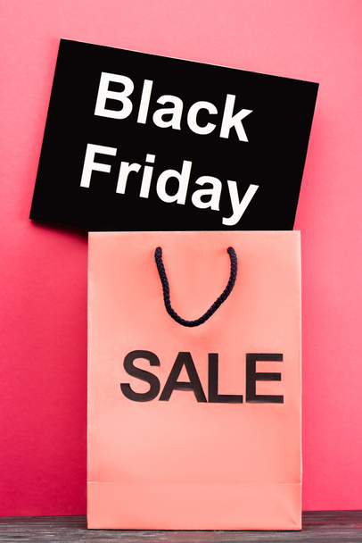 placard with black friday lettering near shopping bag on pink - Photo, Image