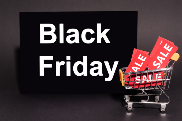 placard with black friday lettering near toy cart with sale tags on dark background  - 写真・画像