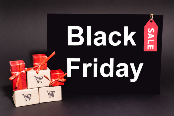 gifts near small carton boxes near placard with black friday lettering on dark background - Photo, Image