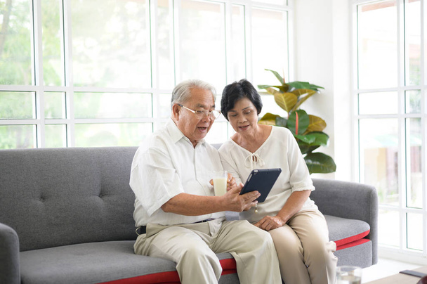A happy senior Asian couple is using tablet and talking with family on webcam at home, retirement concept. - Fotografie, Obrázek