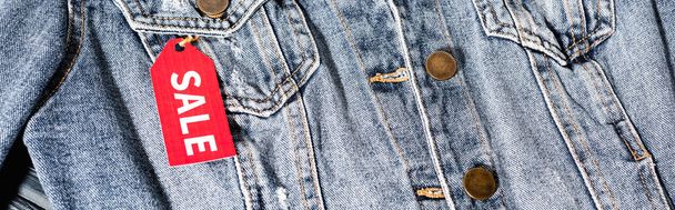 primer plano de etiqueta de venta roja en chaqueta de mezclilla azul, cultivo panorámico  - Foto, Imagen