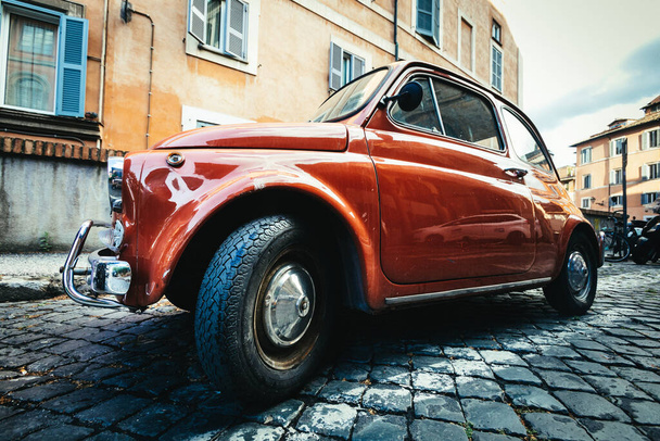 Old compact Italian car Fiat 500 Cinquecento parked in the historic center of Rome in Italy. Orange color, paving with cobblestones. - Fotoğraf, Görsel