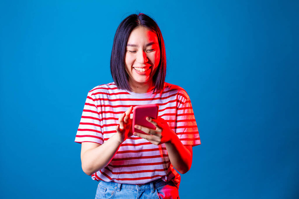 Молодая красивая азиатская женщина смс смартфон на синем фоне - Изолированная азиатская молодая женщина с помощью смартфона улыбаясь студийный снимок - социальная сеть, технологии, концепция разнообразия - Фото, изображение