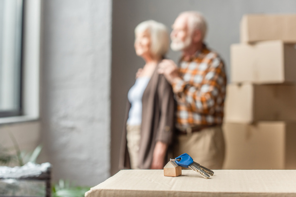 blurred view of senior couple moving into new house and keys on foreground - Photo, Image