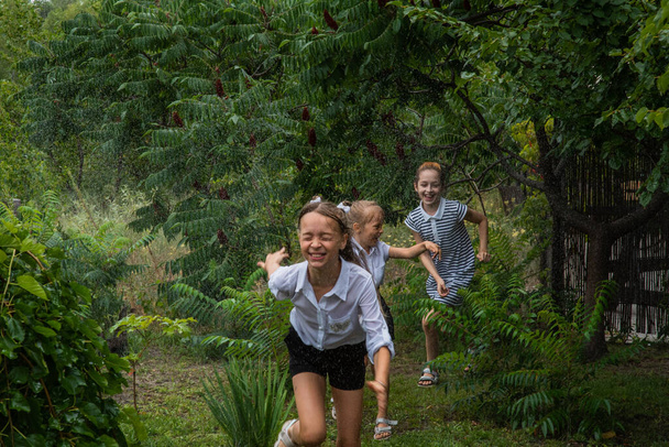 Tři školačky v dešti. Školačky běhají v dešti za teplého počasí. Tři přítelkyně - Fotografie, Obrázek