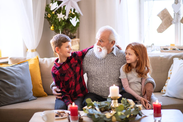 Small children with senior grandfather indoors at home at Christmas, talking. - Valokuva, kuva
