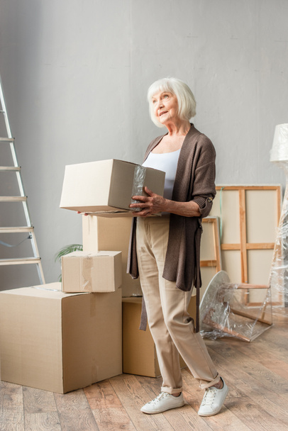 full length view of senior woman holding cardboard box, moving concept - Photo, Image