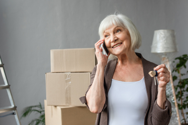 šťastný senior žena mluví po telefonu a drží klíče v novém domě, pohybující se koncept - Fotografie, Obrázek