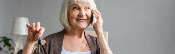 panoramic shot of happy senior woman talking on phone and holding keys in new house, moving concept - 写真・画像