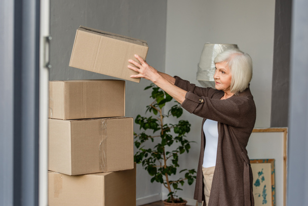 cheerful senior woman arranging cardboard boxes, moving concept - Photo, Image