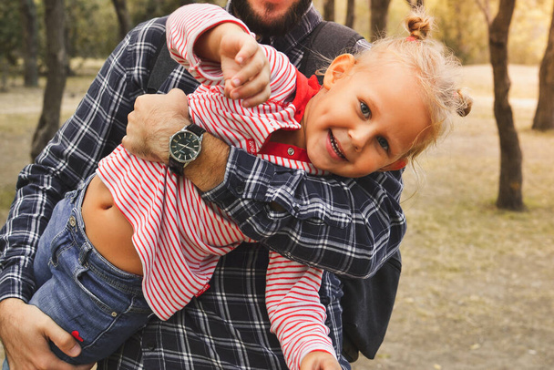 Dziecko przytula tatę. Ojciec trzyma słodką dziewczynkę w ramionach. Jesienny portret dziecka. Szczęśliwa rodzina i chwile dzieciństwa. - Zdjęcie, obraz