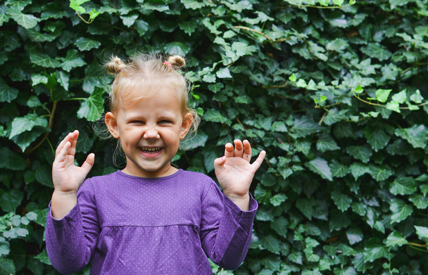 Porträt eines schönen Kindes vor einem Hintergrund aus grünen Blättern. Das Kind lächelt in die Kamera. - Foto, Bild