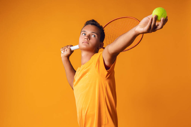 Studio shot of a young tennis player holding racket against orange background - Photo, Image