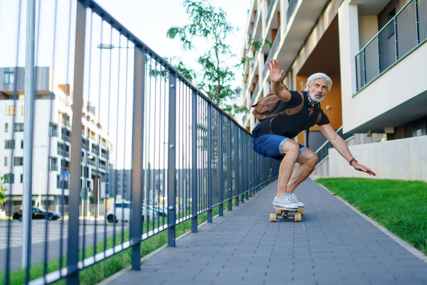 Portrait of mature man riding skateboard outdoors in city, going back to work. - Fotografie, Obrázek
