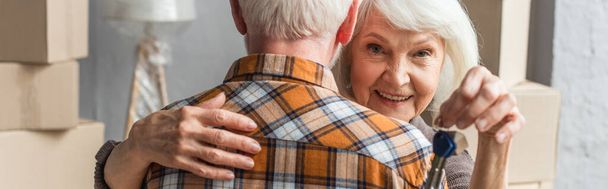 tiro panorâmico de sorrir mulher idosa segurando chaves e abraçando o marido, conceito em movimento - Foto, Imagem