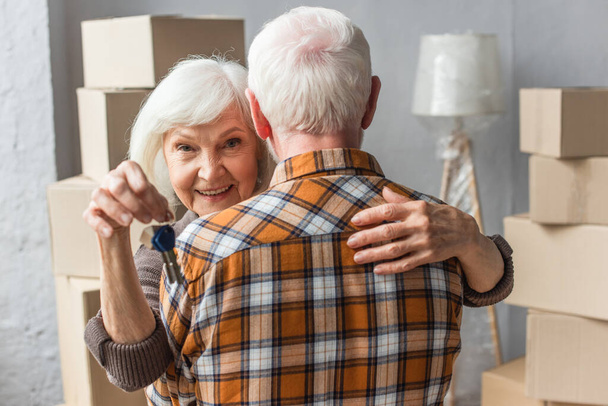 usmívající se starší žena držící klíče a objímající manžel, pohyblivý koncept - Fotografie, Obrázek