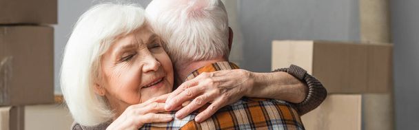 panoramiczne ujęcie starszej kobiety z zamkniętymi oczami przytulającej męża w nowym domu, poruszająca się koncepcja - Zdjęcie, obraz