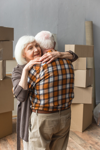 mujer mayor con los ojos cerrados abrazando marido en casa nueva, concepto móvil - Foto, imagen