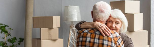 panoramic shot of senior woman with closed eyes hugging husband in new house, moving concept - Photo, Image