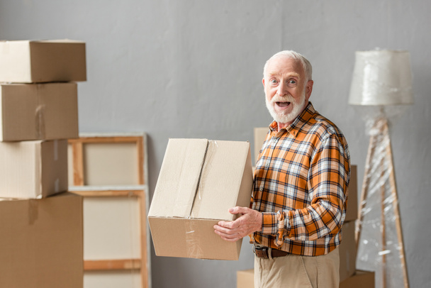 surprised senior man holding cardboard box in new house, moving concept - Photo, Image