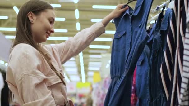 Young woman is buying denim sundress in shopping mall - Footage, Video
