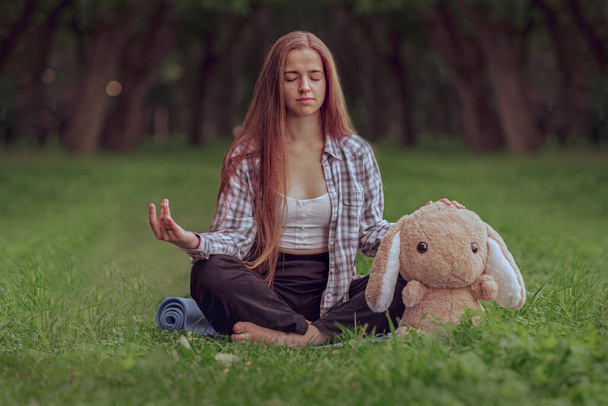 portrait of a young woman practicing yoga in the park on the grass, lotus position, relaxation and meditation concept - Photo, image