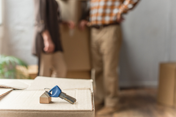 keys lying on cardboard box on foreground and blurred view of senior couple, moving concept - Photo, Image