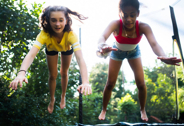 Front view of young teenager girls friends outdoors in garden, jumping on trampoline. - Φωτογραφία, εικόνα