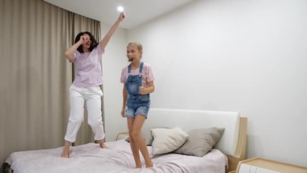 Щаслива молода мама і мила маленька дочка танцює, стрибає в ліжко, сміється мама грає з чудовою підлітковою дитиною в спальні, весела сімейна активність вдома, розважається
 - Кадри, відео