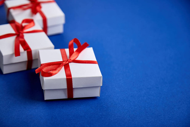 Luxuriöse weiße Geschenkboxen mit rotem Band auf blauem Hintergrund. Valentinstag, Weihnachten, Geburtstagsgeschenke. Vatertag. Flach lag er. Kopierraum. Ansicht von oben. - Foto, Bild