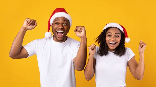 Schwarzes Paar in Weihnachtsmützen schüttelt Fäuste über gelbem Hintergrund - Foto, Bild