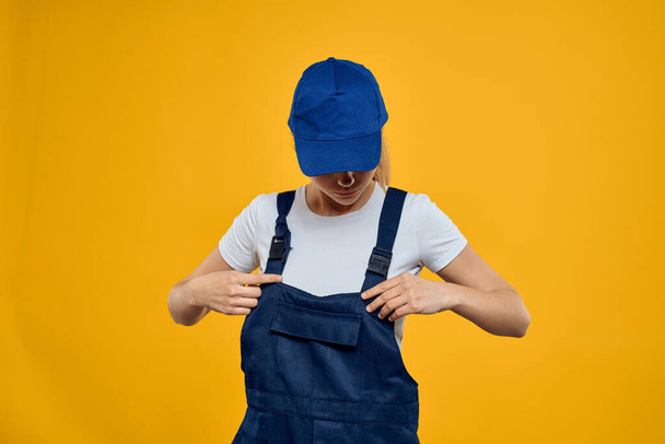 Woman in working uniform blue cap delivering courier service yellow background - Foto, Imagem