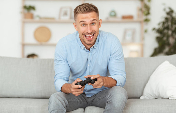 Young guy sitting on couch playing video games - Foto, afbeelding