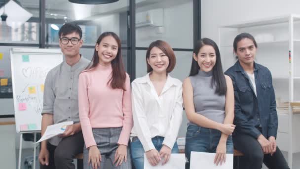 Группа азиатских молодых творческих людей в нарядной повседневной одежде улыбается и поднимает большие пальцы на креативном офисном рабочем месте. Разнообразные азиатские мужчины и женщины стоят вместе в стартапе. Концепция коллективной работы. - Кадры, видео