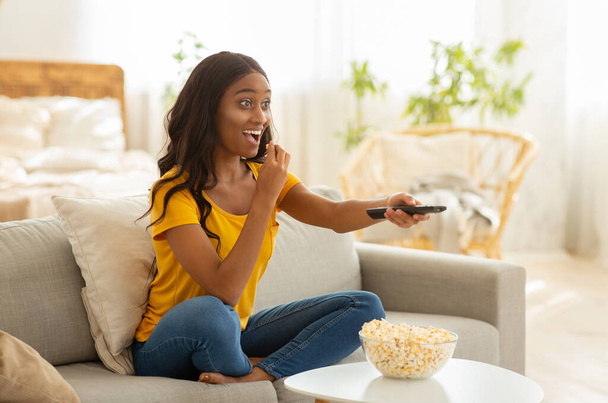 TV kumandalı güzel Afro-Amerikalı kadın evde ilginç bir film seyrediyor, boş bir yer. - Fotoğraf, Görsel