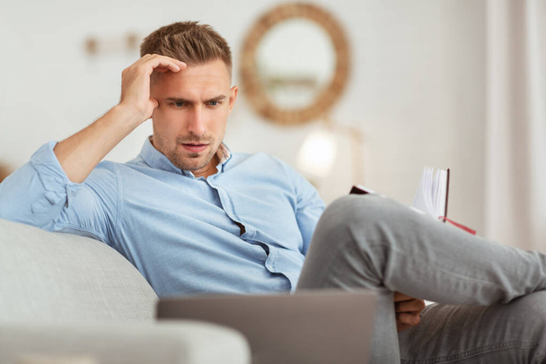 Portrait of pensive man sitting on couch using pc - Photo, Image