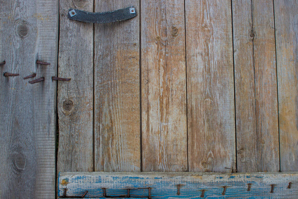 Parte di una vecchia porta di legno con una maniglia di stoffa inchiodata con chiodi arrugginiti. Con una tavola di legno in fondo. - Foto, immagini