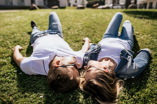 Close up of stylish couple smiling and look at each other lying on green grass - Photo, Image