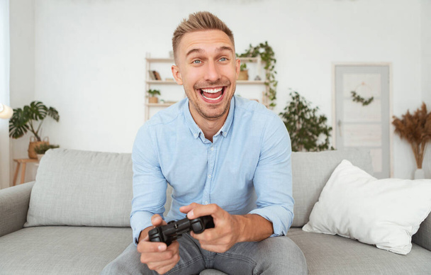 Young guy sitting on sofa playing video games - Foto, afbeelding