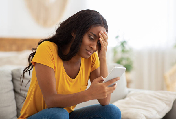 Unhappy African American lady looking at her smartphone with disgust indoors, copy space - Foto, Imagem